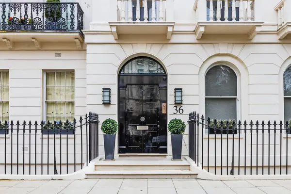 Siyah kapısı, demir parmaklıkları, kemerli pencereleri ve dekoratif bitkileri olan zarif bir Londra konağı girişi..