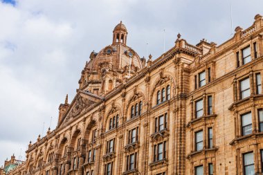 Londra 'daki Harrods' un çarpıcı dış görünüşü, tarihi mimarisi ve bulutlu gökyüzünün altında detaylı görünüşü. Londra, İngiltere, 7 Nisan 2024