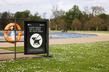 Suyun yanındaki park tabelasında, ziyaretçilere köpekleri yakınlarda yaşam halkası güvenlik ekipmanlarıyla birlikte tutmaları tavsiye ediliyor. Londra, İngiltere, 7 Nisan 2024