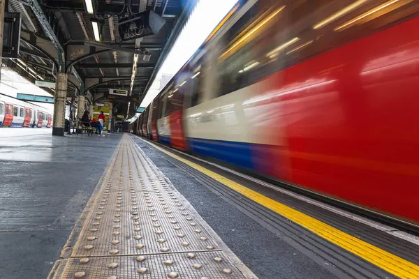 Bir Londra metro treni istasyona hareket halinde girer, açık platform güvenlik işaretleriyle..