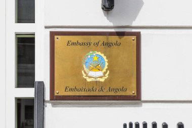 Beyaz bir duvarda ulusal amblem olan Angola Büyükelçiliği pirinç plaketi, resmi diplomatik tabela. Londra, İngiltere, 14 Nisan 2024