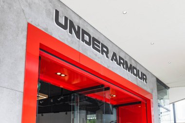 Under Armour mağazasının dış cephesinde koyu kırmızı giriş ve marka tabelaları var. Londra, İngiltere, 14 Nisan 2024