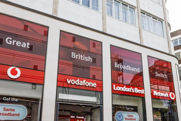 Cesur kırmızı markalaşma, büyük pencereler ve modern tanıtım tabelaları olan bir şehirde Vodafone perakende mağazası. Londra, İngiltere, 14 Nisan 2024