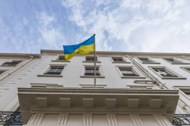 Blue and yellow Ukrainian flag flutters atop a classic white facade, symbol of freedom and national pride, shot from low angle against bright sky.