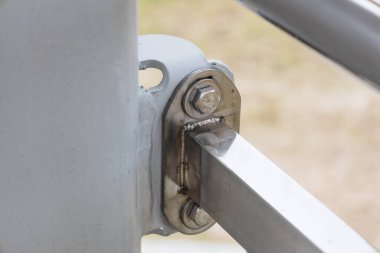 Açık bir çitin üzerindeki yıpranmış metal menteşe eklemlerinin yakın görüntüsü, ayrıntılı cıvatalar ve paslı elementler gösteriyor ki bu yıllar süren maruz kalma ve endüstriyel kullanımı gösteriyor..