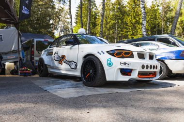 Geniş çamurlukları, derin bulaşık tekerleri ve agresif havacıları olan ağır modifiye edilmiş beyaz BMW drift araba yarışmadan önce orman çayırlarında dinleniyor. Alytus, Litvanya, 25 Mayıs 2025