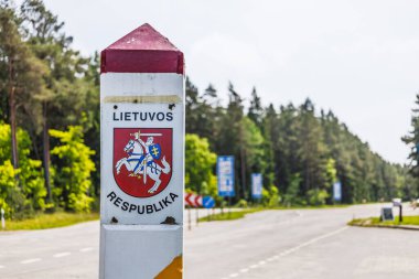 Litvanya arması taşıyan beyaz kırmızı sütun güneşli bir orman yolunda ulusal sınırı işaret ediyor. Seyahat gazeteciliği, Avrupa siyaseti, Schengen veya yol gezisi görselleri için ideal