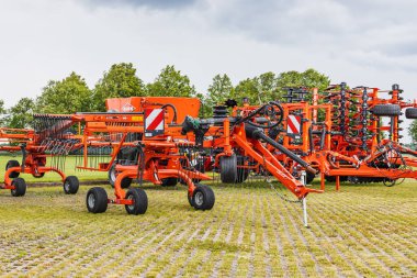 High capacity red seed drill with integrated cultivator on rural dealership yard. Wheels, discs, hopper and hoses visible beneath cloudy sky. Kaunas, Lithuania, 19 June 2025