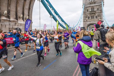Londra Maratonu 2024. Tower Köprüsü 'nde koşan beş gönüllü, renkli yardım önlükleri, tezahürat yapan kalabalık. Londra, İngiltere, 21 Nisan 2024