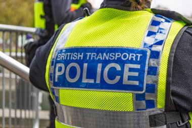 İngiliz Ulaştırma Polisi yamasıyla sarı yeleğin ayrıntılı görüntüsü, demiryolu güvenliği ve İngiliz istasyonları arasındaki kamu güvenliğini simgeliyor.