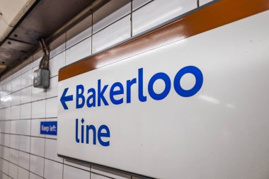 Bakerloo Hattı tabelasını mavi metin ve okla kapatın. Londra metrosundaki beyaz fayanslar üzerinde, yolculara platforma kadar rehberlik ediyor..