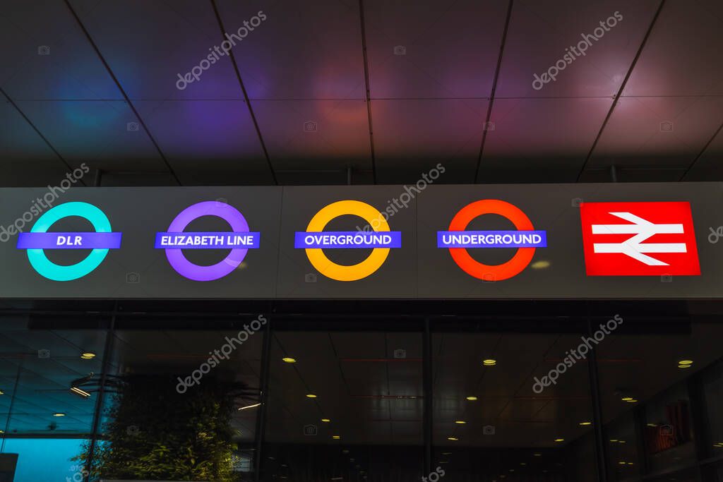 Neon London Underground roundels in vivid line colours plus red National Rail logo shine over a station entrance, celebrating UK transit branding after dark. London, UK, 5 May 2024