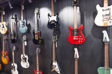 Çağdaş bir müzik dükkanının karanlık bir sergi duvarında canlı kaplamalı elektro ve bas gitarlar asılı. Londra, İngiltere, 11 Mayıs 2024