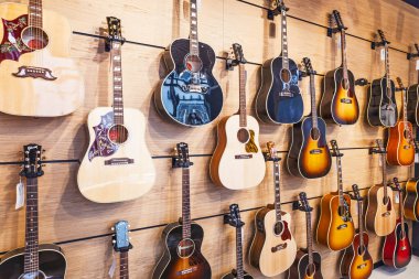 Ahşap tahta duvarda çeşitli akustik ve elektrikli gitarların geniş açılı çekimi, müzikal perakende ve yaratıcı ilham temaları için mükemmel. Londra, İngiltere, 11 Mayıs 2024