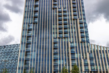 Çizgili mavi pencereleri ve altın yüzgeçleri olan parlak cam gökdelenler, balkonları ve kara kara kara düşünen fırtına bulutları tarafından çerçevelenmiş dikey çizgiler..