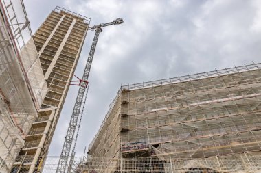 Yüksek bina iskeletinin alçak açılı fotoğrafı ve bulutlu bir gökyüzünün altında geniş bir iskeletle çerçevelenmiş kule vinci. Londra, İngiltere, 1 Haziran 2024