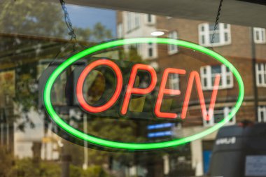 Dükkan vitrininde ışıklı neon ışıklı açık tabela. Yeşil oval sınır, kentsel yansımalar, iş saatlerinin sembolü ve müşteri memnuniyeti.