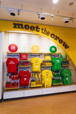 M ve M - Mürettebatla tanışın - duvar, kırmızı, sarı ve yeşil karakterli tişörtler Leicester Meydanı amiral gemisi mağazasındaki parlak sarı kemerin altında. Londra, İngiltere, 2 Haziran 2024