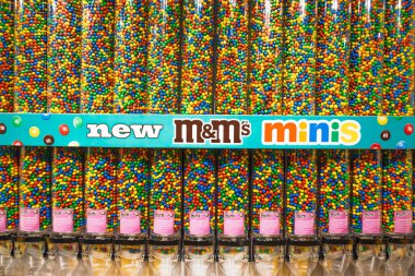 M ve M minis toplu şeker kutusu duvarı gökkuşağı çikolata boncukları, turkuaz pankart ve bayrak gemisi şeker dükkanında pembe paraşüt ile dolu. Londra, İngiltere, 2 Haziran 2024