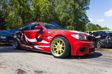 Göz alıcı kırmızı BMW drift araba neon tekerlekler ve vahşi sargı güneşli çayırda oturur. Alytus, Litvanya, 25 Mayıs 2025