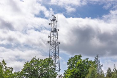 Kırsaldaki çiçek açan ağaçların üzerinde bulunan uzun kafes baz istasyonu parçalı bulutlu gökyüzünün altında 4G-5G kapsama alanı sağlıyor..