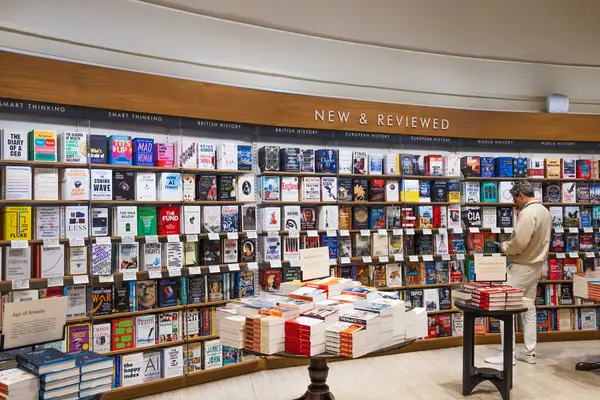 Waterstones kitapçısının içinde Yeni ve Moda bir duvar, renkli kapaklar, en çok satanlar tabloları ve gezen bir müşteri var. Londra, İngiltere, 8 Haziran 2024