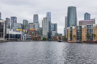 Canary Wharf finans bölgesinin sakin rıhtım suları, modern cam gökdelenler, ofisler ve bulutlu gökyüzü altındaki daireler geniş görüşlü. Londra, İngiltere, 9 Haziran 2024