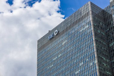 Şirket logosuna sahip cam ofis gökdelenleri yansıtıcı pencereler ve mavi gökyüzü bulutları. Londra, İngiltere, 16 Haziran 2024
