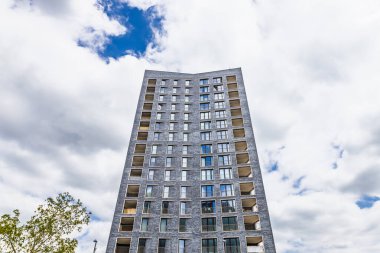 Bulutlu bir gökyüzünün altında, geometrik pencereleri ve balkonları olan modern, yüksek açılı bir konut kulesinin alçak açılı görüntüsü..