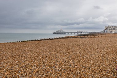 Eastbourne İskelesi, gri bulutların altında geniş bir sahil boyunca uzanır. Sussex kıyısındaki klasik İngiliz sahili.