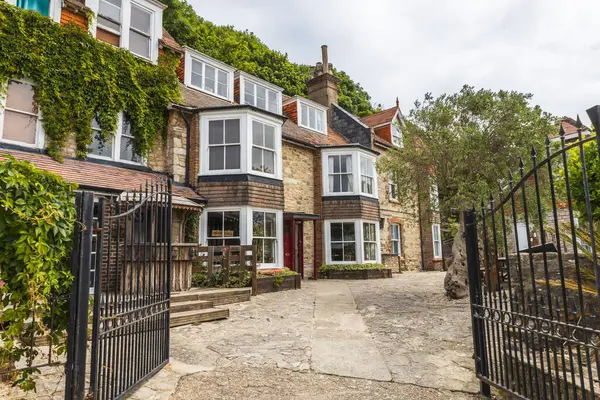 Ivy koyu pencereli, taş kaldırımlı ve işlenmiş demir kapılı İngiliz kır evi cephesini örttü..