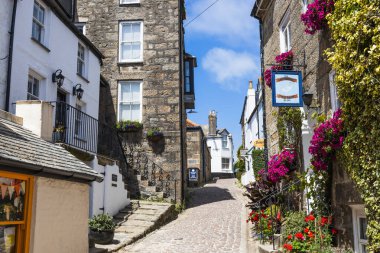St. Ives, Cornwall 'daki eski püskü patika. Beyaz boyalı kulübeler, granit duvarlar ve mavi bir gökyüzünün altında canlı sepetlerle dolu. St Ives, İngiltere, 4 Temmuz 2024