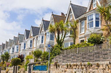 Şık İngiliz kıyı evleri güneşli bir yamaçta, taş duvarları, defne pencereleri, gable çatıları ve parlak mavi gökyüzü altında palmiye çizgili ön bahçeleri olan..