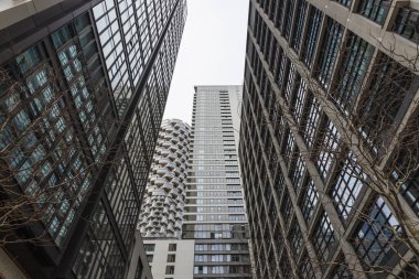 Modern ofis gökdelenleri, vitrin camları, çelik ve şehir merkezindeki hareketli bir iş koridorunda yoğun şehir mimarisi arasında çarpıcı bir yükseliş perspektifi..