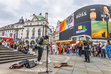 Piccadilly Circus, Londra 'da canlı bir gün sahnesi. Eros Fountain 'in yanındaki sokak müzisyeni, seyirciler ve tarihi West End' deki parlak dijital reklam panoları. Londra, İngiltere, 21 Mayıs 2023