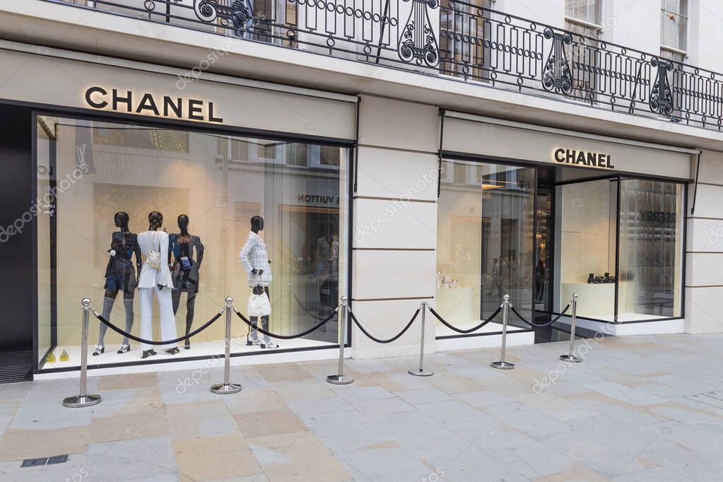 Exterior of a Chanel boutique with sleek facade, glowing signage, and refined mannequins in a minimalist window display on an upscale shopping street. London, UK, 21 May 2023