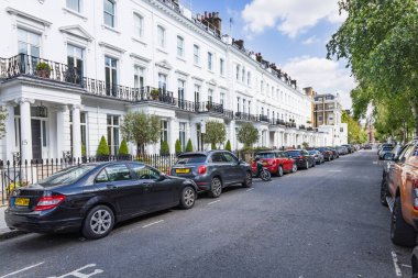 Beyaz viktorya dönemi konakları, park halindeki arabaları, demir korkulukları ve parlak mavi gökyüzünün altında yapraklı ağaçları olan sessiz bir Londra caddesini hizaya sokuyor. Londra, İngiltere, 24 Mayıs 2023