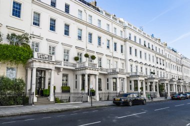 Saf mavi bir gökyüzü altında sessiz, lüks bir yerleşim sokağında portico sütunları ve demiryolu döşeme demirleri olan zarif, beyaz Londra evlerinin olduğu sıra. Londra, İngiltere, 27 Mayıs 2023