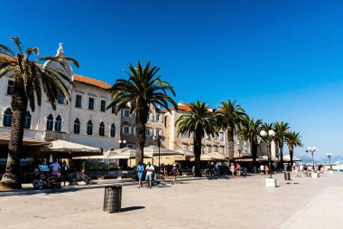TROGIR, CROATIA - 30 Ekim 2022: Trogir kasabasında restoranlar ve palmiye ağaçları olan gezinme alanı.