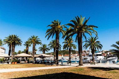TROGIR, CROATIA - 30 Ekim 2022: Eski Trugir kasabasında yatları ve palmiye ağaçları olan gezinme alanı.