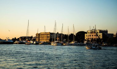 ZADAR, CROATIA - Kasım 02, 2022: Şehrin diğer tarafındaki binalar ve teknelerle gün batımında manzara.