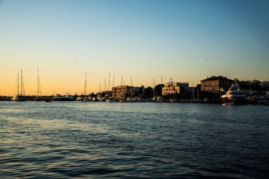 ZADAR, CROATIA - Kasım 02, 2022: Şehrin diğer tarafındaki binalar ve teknelerle gün batımında manzara.
