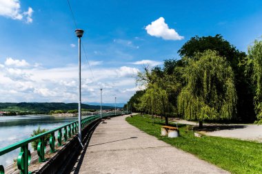 Jiu Nehri 'nin yanındaki Targu Jiu Central Park' taki ara sokak ve arkada da Ferdinand Köprüsü olarak da bilinen Jiu Nehri üzerindeki eski köprü var. Targu jiu, Romanya.