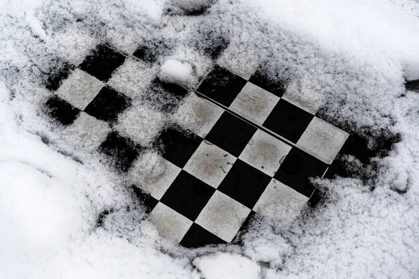Outdoor chess board covered with snow.