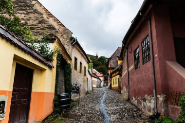 SIGHISOARA, ROMANIA - 23 Eylül 2022: Renkli evleri olan eski ortaçağ sokağı ve arka planda tepenin üzerindeki kilise.