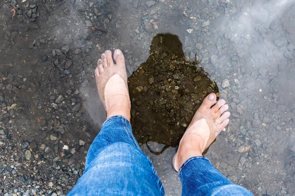 Woman\'s legs in jeans with bare soles standing in water.