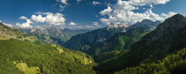 Arnavutluk 'un muazzam Alpleri' nin panoramik ve havadan görünüşü. Yürüyüş yolları, bulutlu koyu mavi gökyüzü, dik kayalar, yeşil vadi, kar kalıntıları, yaz. Theth Ulusal Parkı, Arnavutluk Alpleri, Arnavutluk.