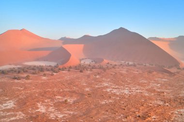 Uçsuz bucaksız turuncu kum tepelerinin şekilleri ve gölgeleri yükselen güneşle aydınlanıyor. Namib-Naukluft Ulusal Parkı 'nın Çöl manzarası, Namibya.