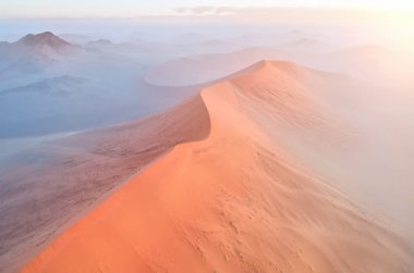 Uçsuz bucaksız turuncu kum tepelerinin şekilleri ve gölgeleri yükselen güneşle aydınlanıyor. Namib-Naukluft Ulusal Parkı 'nın Çöl manzarası, Namibya.