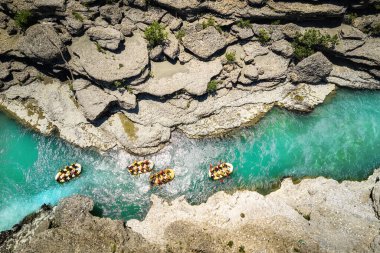 A vertical view of a group of four yellow rafts floating among the rocks on the crystal clear, blue-green water of Vjosa river, Albania.